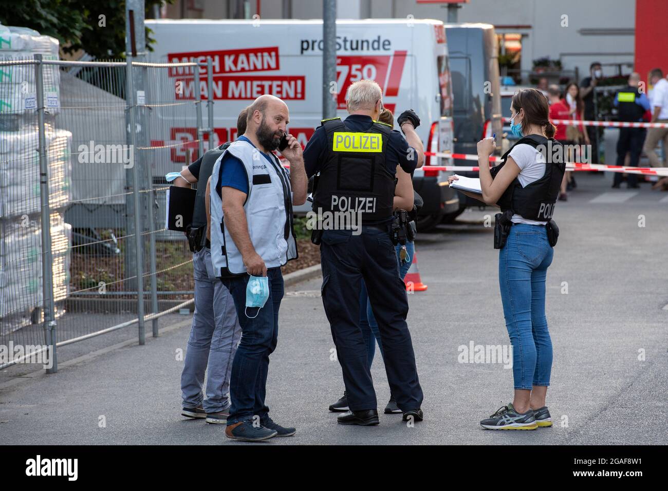 Berlino, Germania. 30 luglio 2021. Gli agenti di polizia si trovano dietro i nastri di protezione nei locali di un negozio fai da te a Berlino-Wedding. Diversi colpi sono stati sparati nel parcheggio nel tardo Venerdì pomeriggio. Secondo il reparto vigili del fuoco, ci sono stati quattro feriti, tre uomini e una donna. Sono stati trattati in loco da medici e poi portati in ospedale, ha detto un portavoce del dipartimento dei vigili del fuoco. La polizia e i vigili del fuoco hanno risposto a un'operazione su larga scala. Credit: Paul Zinken/dpa-Zentralbild/dpa/Alamy Live News Foto Stock