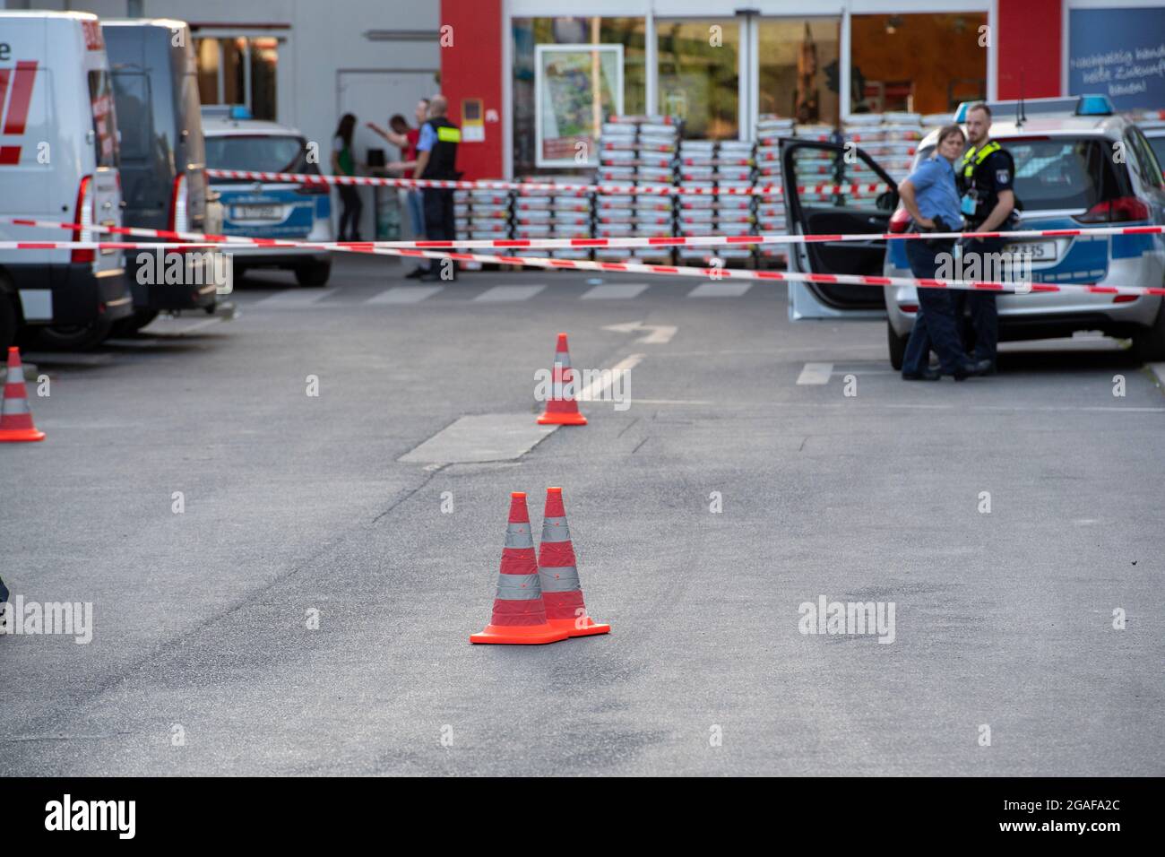 Berlino, Germania. 30 luglio 2021. Gli agenti di polizia si trovano dietro un cordone presso il sito di un negozio fai da te a Berlino-Wedding. Diversi colpi sono stati sparati nel parcheggio nel tardo Venerdì pomeriggio. Secondo il reparto vigili del fuoco, ci sono stati quattro feriti, tre uomini e una donna. Sono stati trattati in loco da medici e poi portati in ospedale, ha detto un portavoce del dipartimento dei vigili del fuoco. La polizia e i vigili del fuoco hanno risposto a un'operazione su larga scala. Credit: Paul Zinken/dpa-Zentralbild/dpa/Alamy Live News Foto Stock