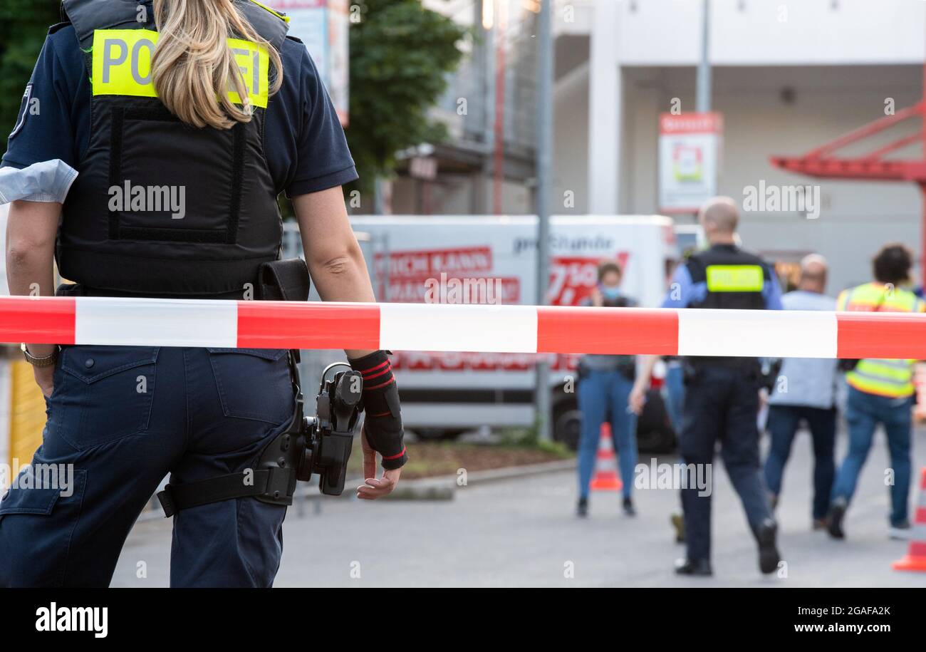 Berlino, Germania. 30 luglio 2021. Gli agenti di polizia si trovano dietro un cordone presso il sito di un negozio fai da te a Berlino-Wedding. Diversi colpi sono stati sparati nel parcheggio nel tardo Venerdì pomeriggio. Secondo il reparto vigili del fuoco, ci sono stati quattro feriti, tre uomini e una donna. Sono stati trattati in loco da medici e poi portati in ospedale, ha detto un portavoce del dipartimento dei vigili del fuoco. La polizia e i vigili del fuoco hanno risposto a un'operazione su larga scala. Credit: Paul Zinken/dpa-Zentralbild/dpa/Alamy Live News Foto Stock