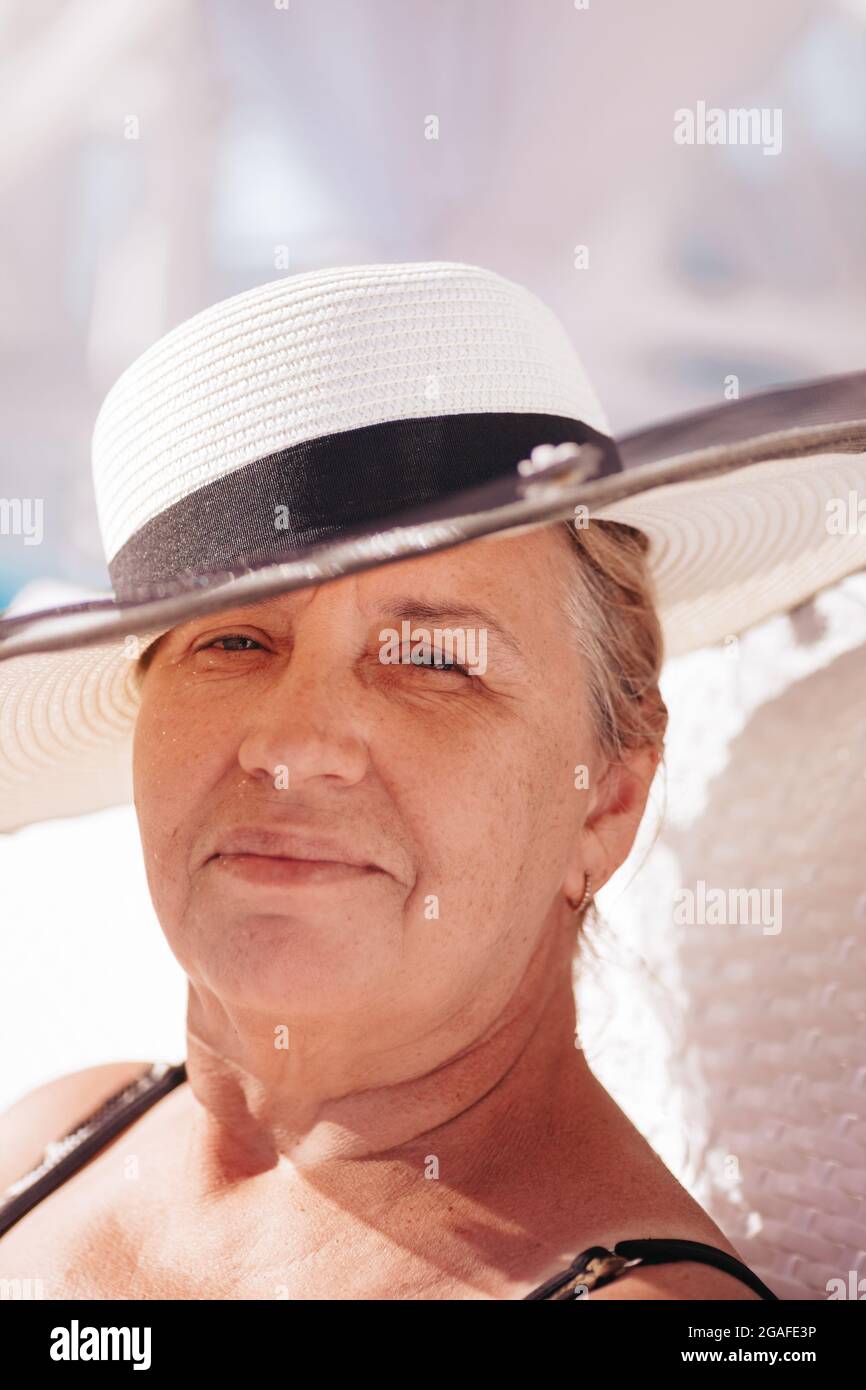 Una donna in un cappello di paglia. Primo piano ritratto di una donna anziana e felice in un cappello di paglia bianca che riposa in un hotel durante le vacanze estive Foto Stock