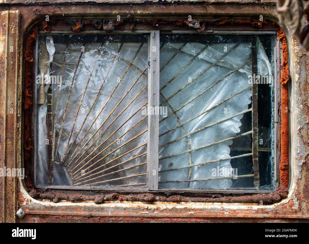 La finestra di un vecchio vagone arrugginito, un rimorchio, con una griglia di ferro e una tenda sporca e strappata Foto Stock
