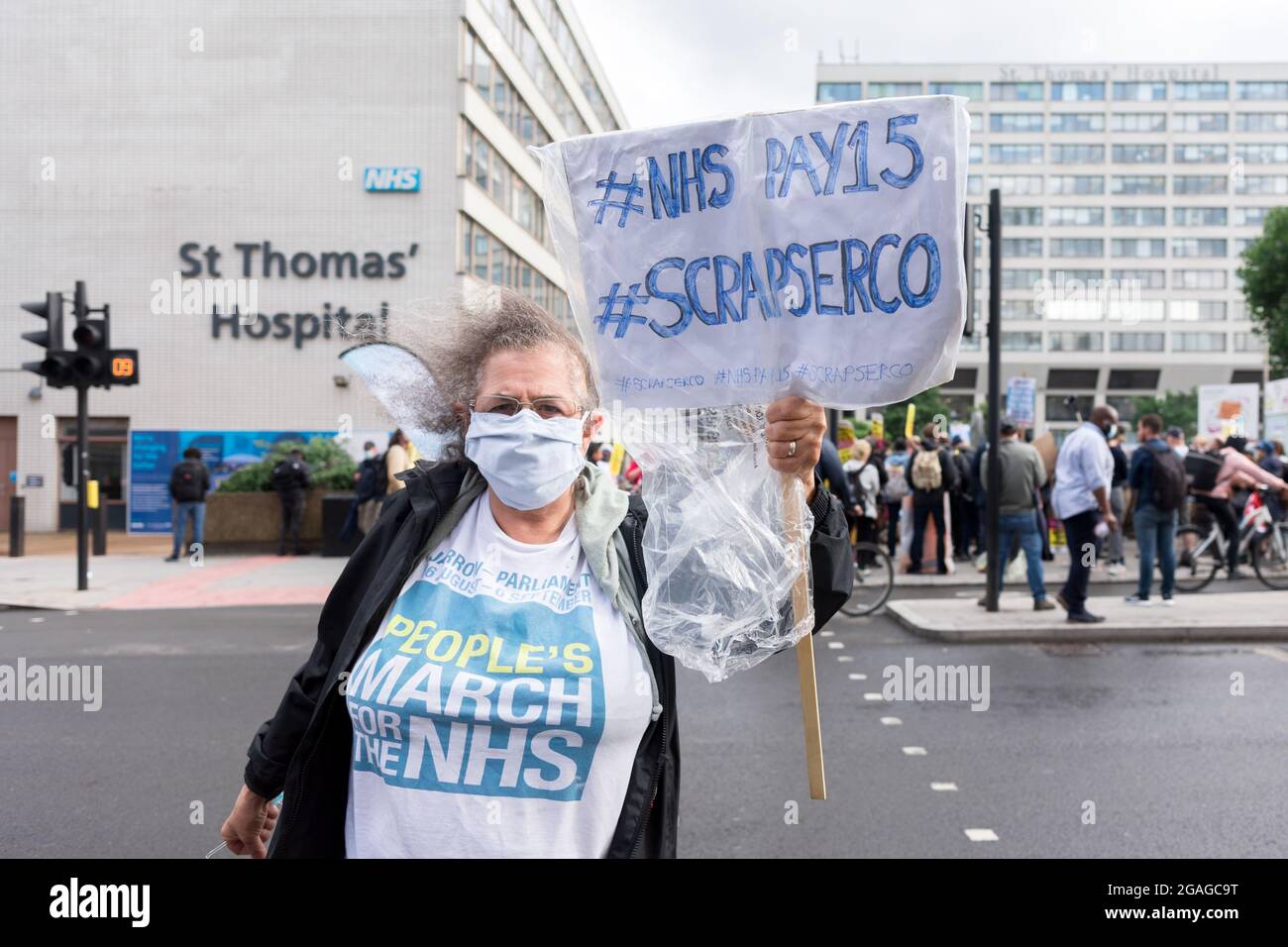 Un'infermiera in pensione che indossa una camicia che dice "marcia del popolo per l'NHS" ha un cartello con la scritta "NHS Pay15, Scrape serco' durante la dimostrazione fuori dall'ospedale St. Thomas'. I membri del Servizio sanitario Nazionale (NHS) si sono riuniti fuori dall'ospedale St. Thomas' prima di marciare verso Downing Street in una dimostrazione che richiede una retribuzione equa per i lavoratori NHS, in quanto l'aumento retributiva del 3% rivisto dal governo è stato ritenuto poco soddisfacente. Le questioni affrontate includevano orari di lavoro lunghi, personale insufficiente e mancanza di materiali di protezione adeguati per gli operatori sanitari. La dimostrazione è stata condotta da lavoratori NHS dicono No, Foto Stock