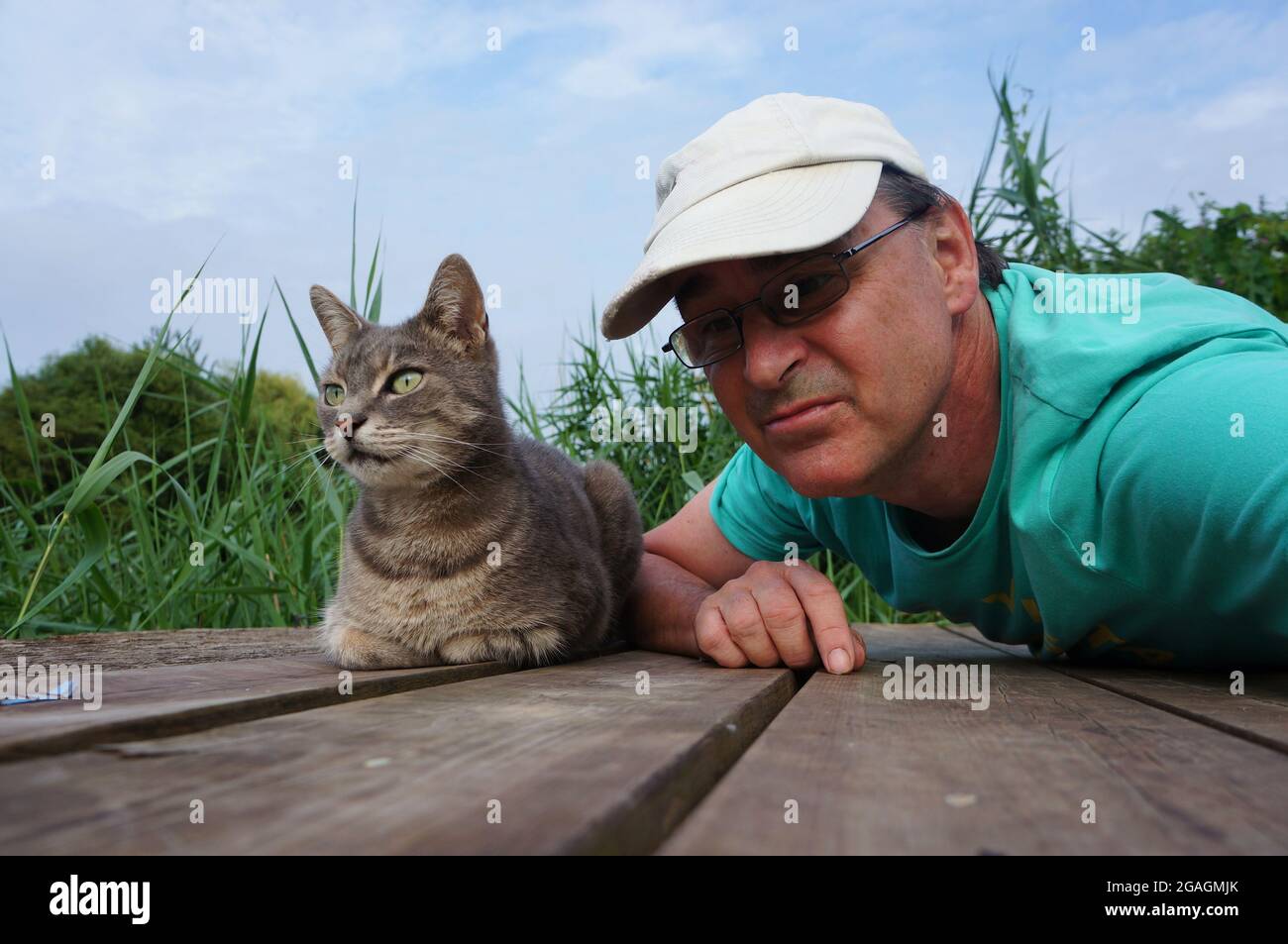 Un uomo con un adorabile gatto tabby su un ponte di legno nel giardino Foto Stock