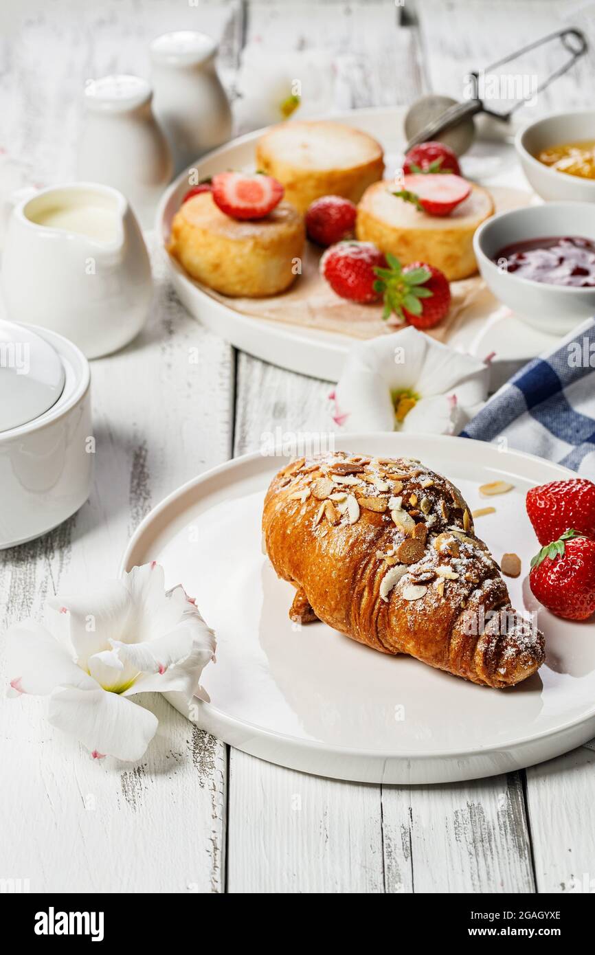 Appetitosi croissant croccanti e frittelle al formaggio di Cottage con fragole fresche e marmellata di frutti di bosco. Colazione deliziosa e sana. Cibo dolce. Woo Foto Stock