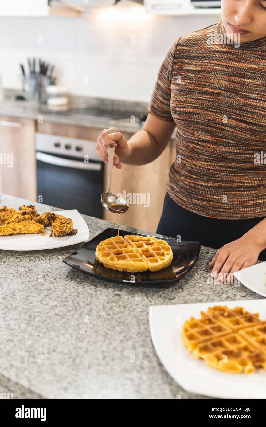 Donna che versa miele e salsa al barbecue sui waffle accanto a bistecche fritte di pollo in pastella di cereali Foto Stock