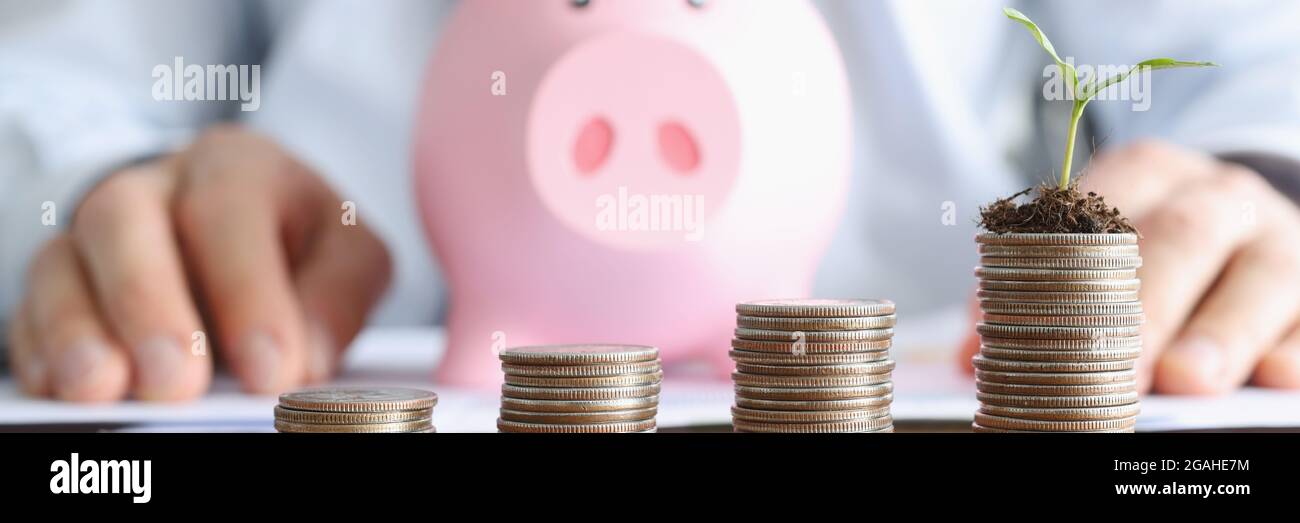 Le torri a moneta ascendenti si trovano sul tavolo contro lo sfondo di una banca di piggy rosa. Foto Stock