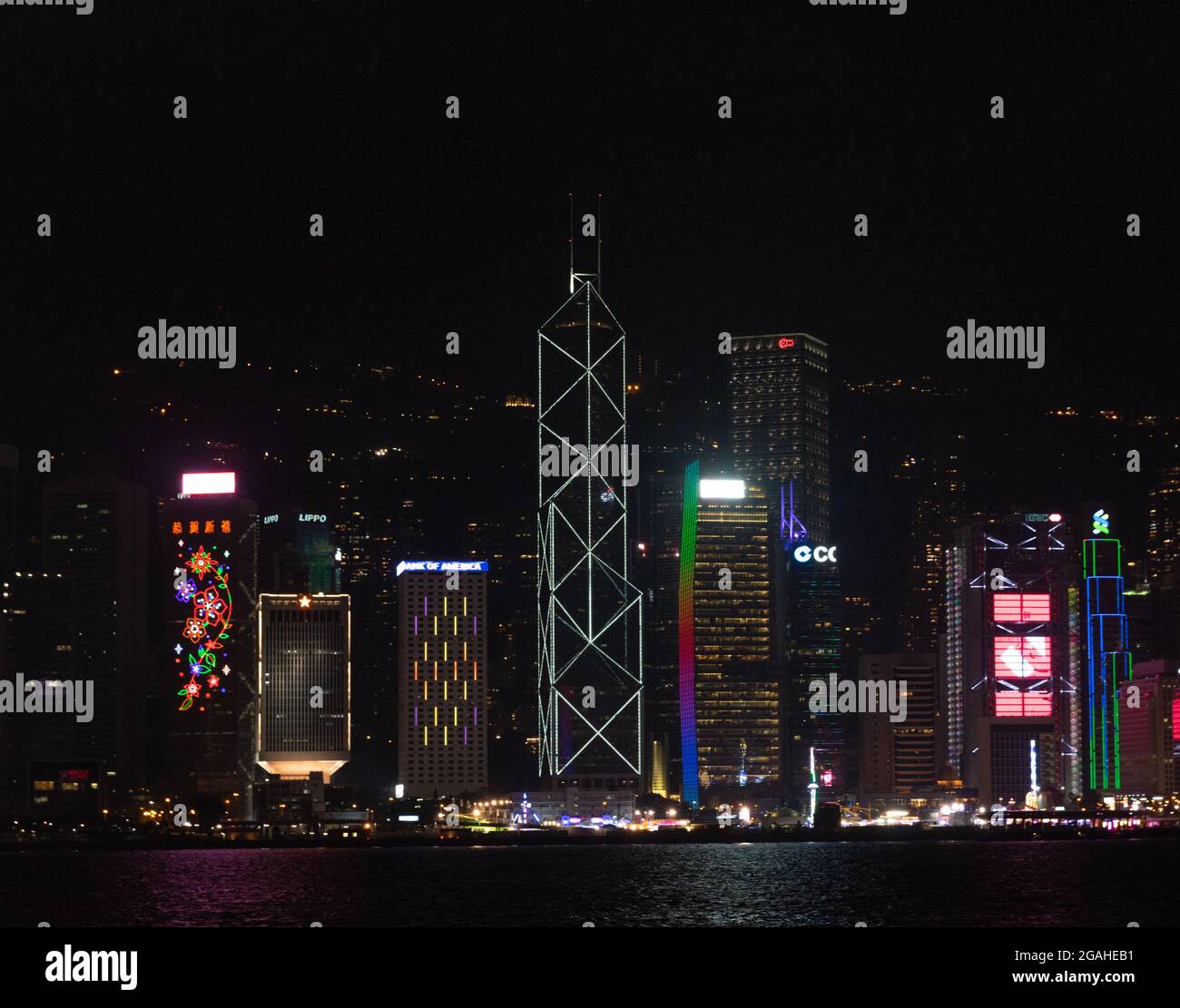 Skyline di Hong Kong con grattacieli illuminati di notte, attraverso il porto di Victoria Foto Stock