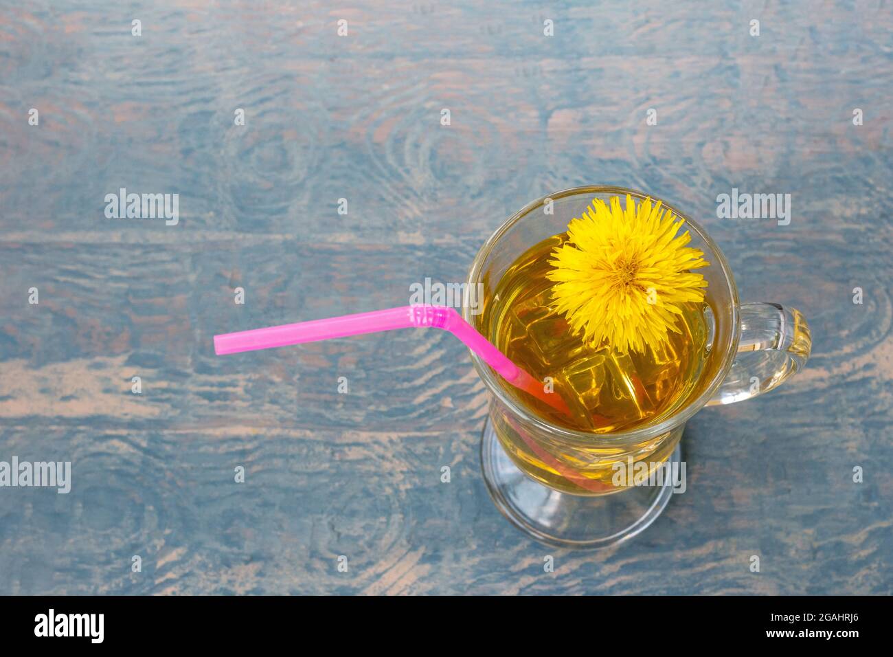 Tazza di tè con tè alle erbe e dente di leone giallo e paglia rosa su sfondo di legno blu illuminato da fascio di sole, spazio copia. Erbe ambientali fr Foto Stock