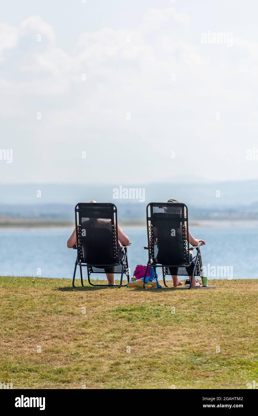 Due persone sedute in sedie al mare, due persone in sdraio in spiaggia,  coppia in pensione che guarda al mare sulla costa Foto stock - Alamy