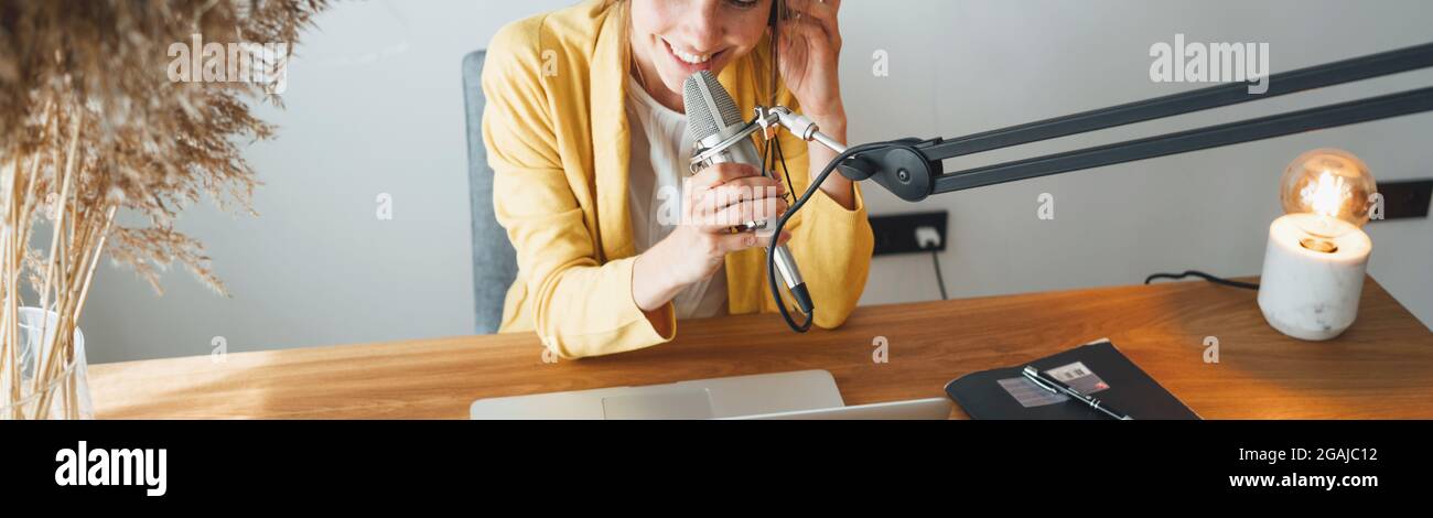 Podcaster donna allegra che registra la sua voce nel microfono. Podcast in streaming di radio host femminile utilizzando microfono e computer portatile nel suo studio di casa. Ampio Foto Stock