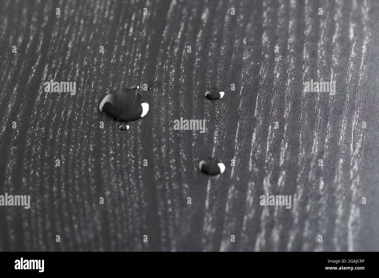 Goccia d'acqua su superficie di legno nero macro vista ravvicinata Foto Stock