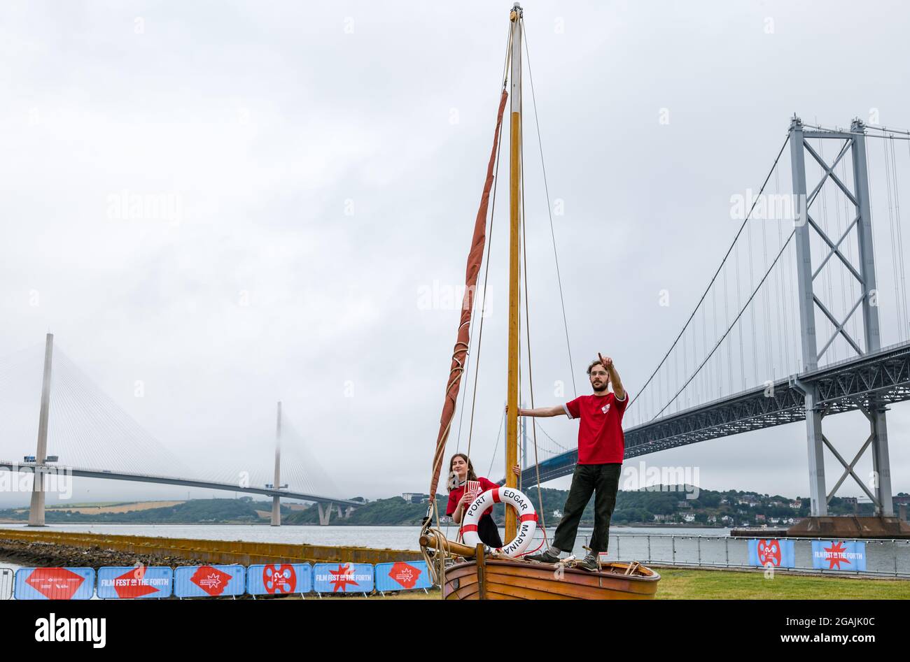 Port Edgar Marina, South Queensferry, Scozia, Regno Unito, 31 luglio 2021. Edinburgh International Film Festival, Film Fest on the Forth: Il porto turistico si trasforma in un cinema all'aperto per un fine settimana di proiezioni gratuite all'aperto, il tutto esaurito. Nella foto: Hannah Knox e Liam Rotheram lanciano il primo giorno da una piccola barca a vela di legno vicino al quarto ponte stradale e Queensferry Crossing Foto Stock