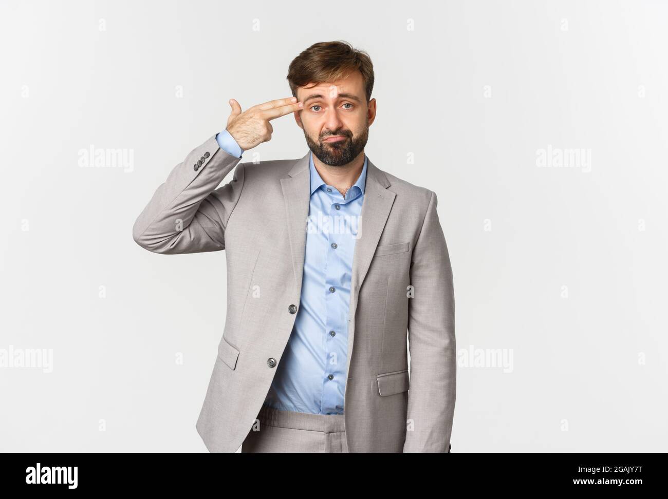 Immagine di un uomo d'affari misero con la barba, indossando il vestito grigio, facendo segno della pistola del dito sulla testa e sparando se stesso, in piedi angosciati su bianco Foto Stock