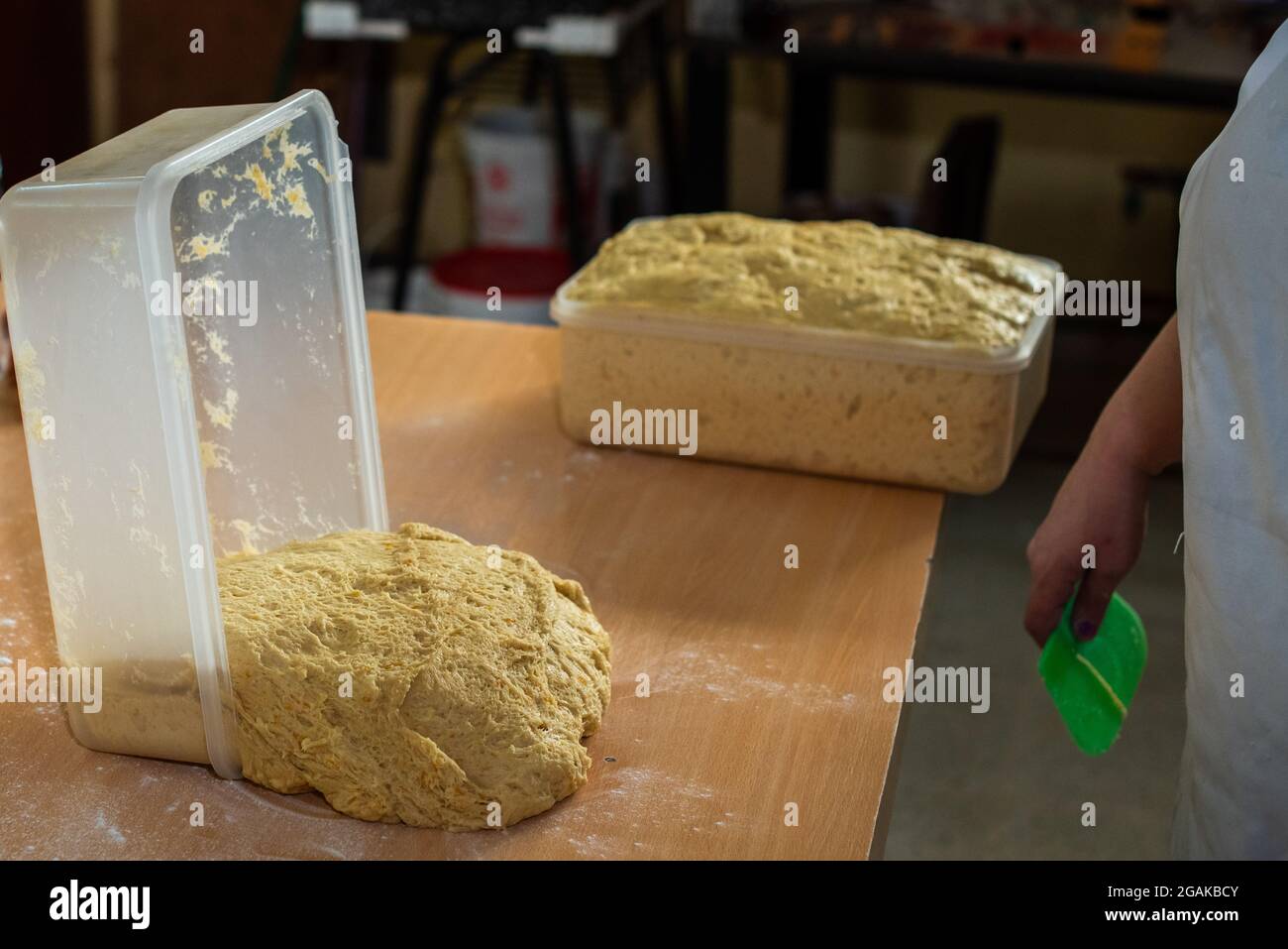 Mujer caucásica masando masa para hacer pan y bizcochos en una mesa color madera con luz de día, en una panadería. Foto Stock