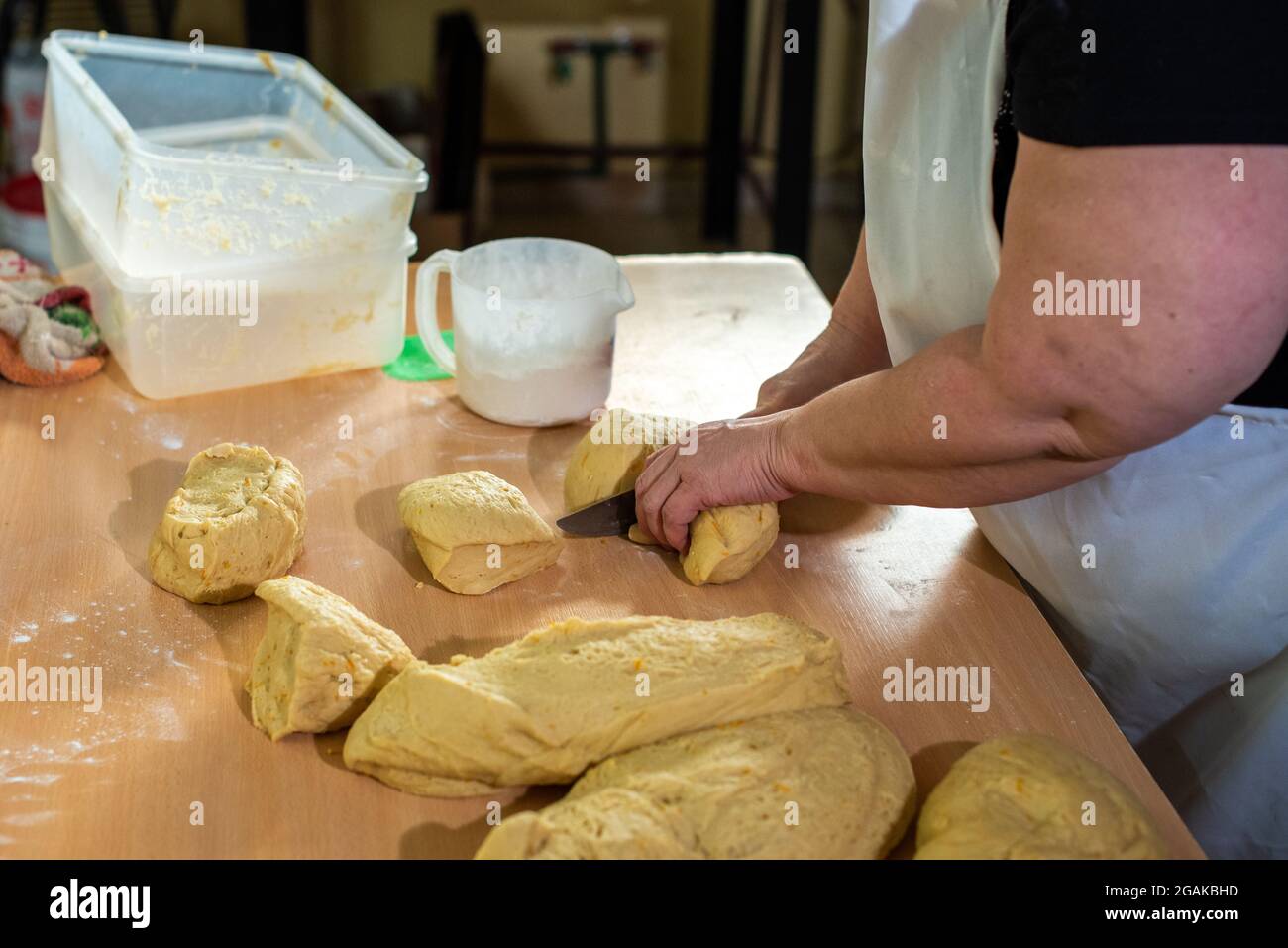 Mujer caucásica masando masa para hacer pan y bizcochos en una mesa color madera con luz de día, en una panadería. Foto Stock