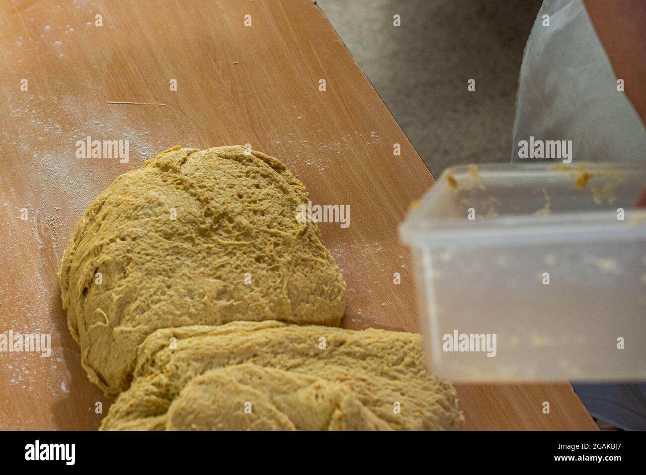 Mujer caucásica masando masa para hacer pan y bizcochos en una mesa color madera con luz de día, en una panadería. Foto Stock