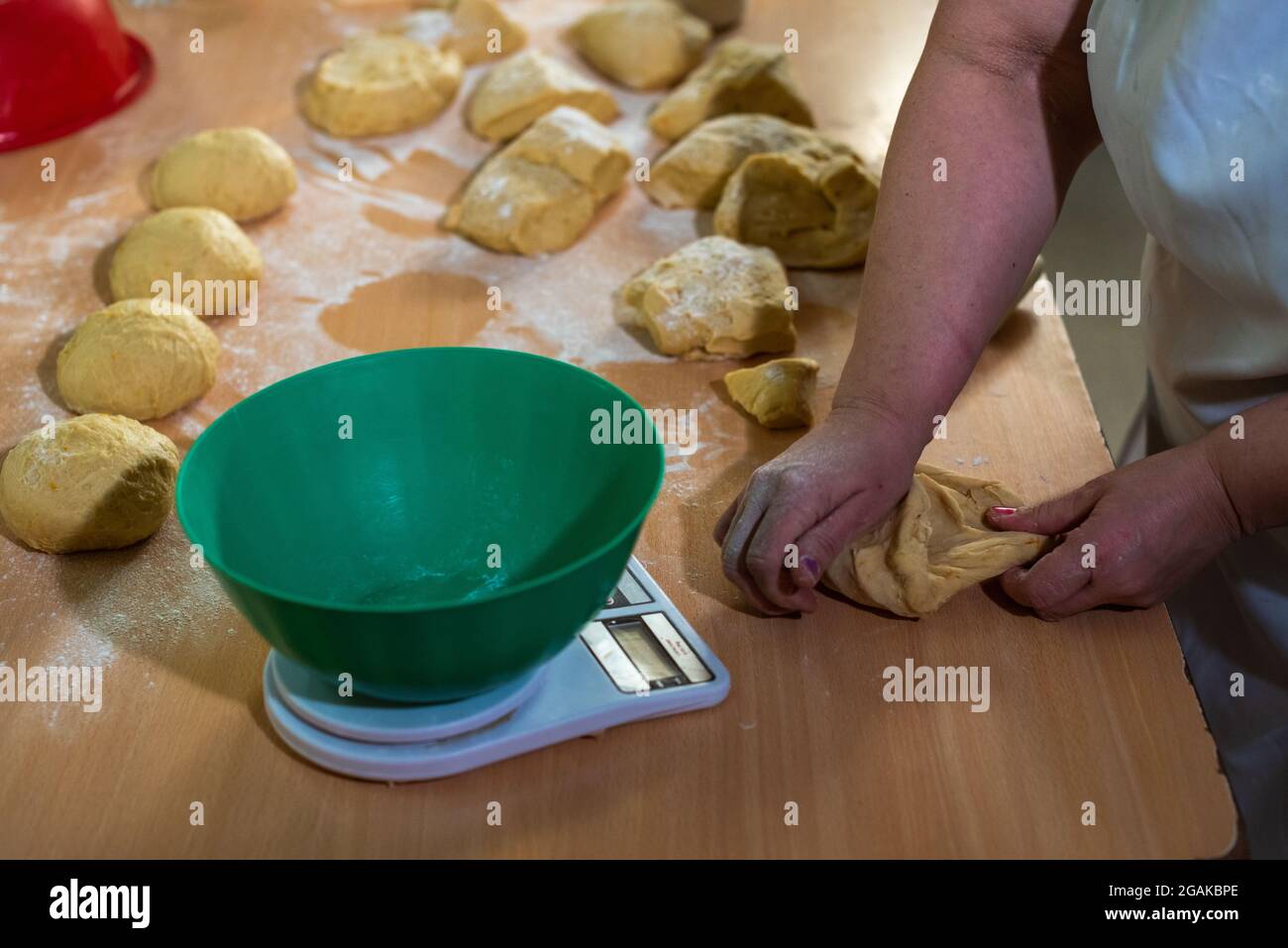 Mujer caucásica masando masa para hacer pan y bizcochos en una mesa color madera con luz de día, en una panadería. Foto Stock