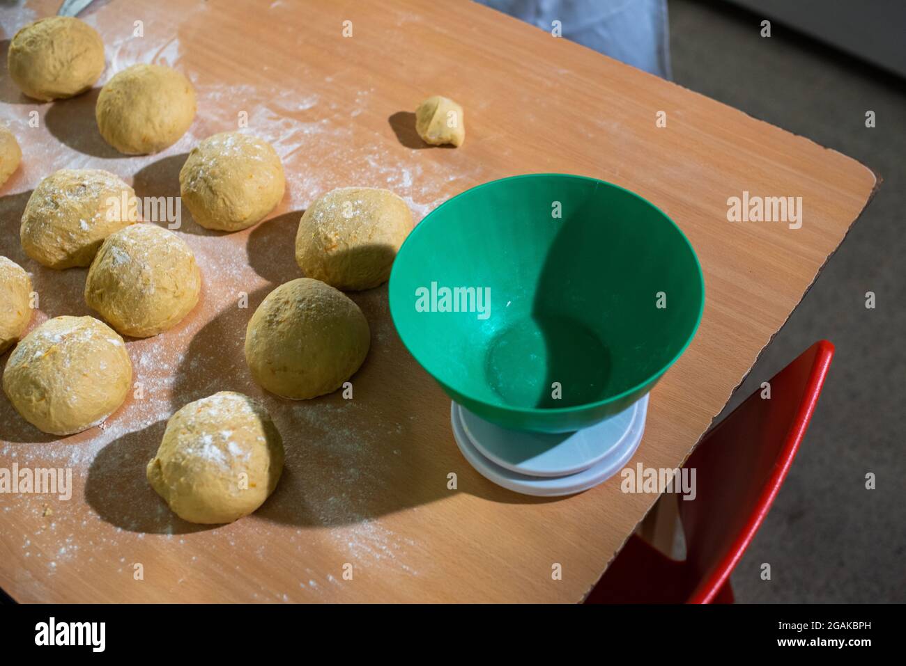 Mujer caucásica masando masa para hacer pan y bizcochos en una mesa color madera con luz de día, en una panadería. Foto Stock