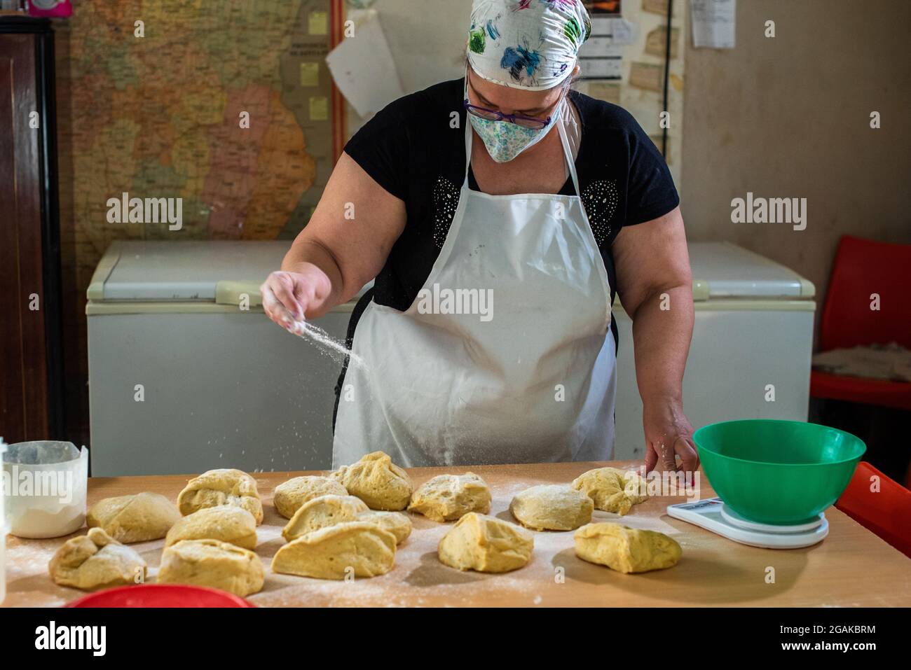 Mujer caucásica masando masa para hacer pan y bizcochos en una mesa color madera con luz de día, en una panadería. Foto Stock
