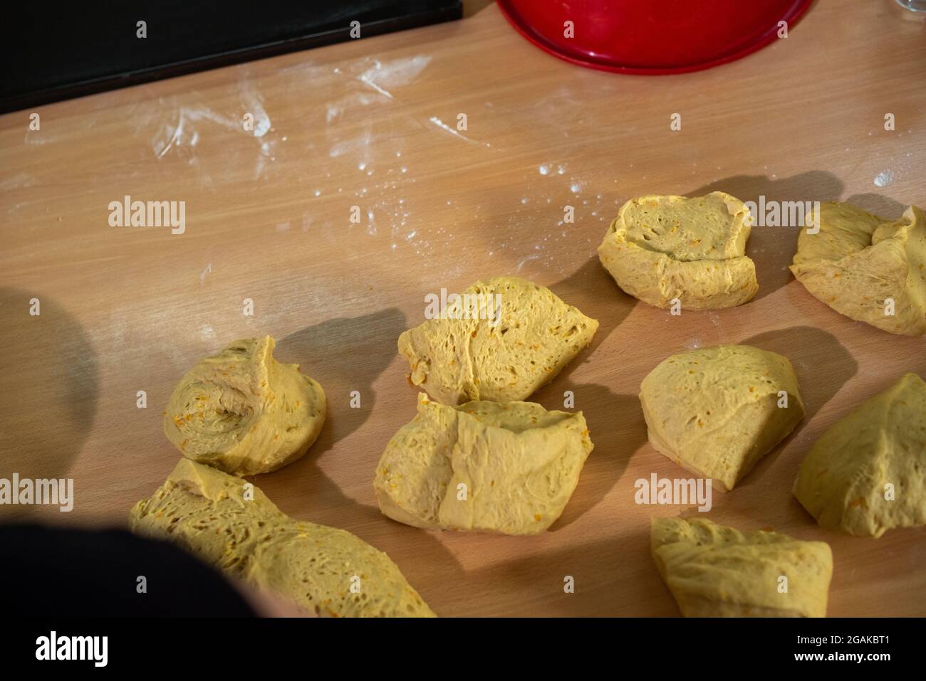Mujer caucásica masando masa para hacer pan y bizcochos en una mesa color madera con luz de día, en una panadería. Foto Stock
