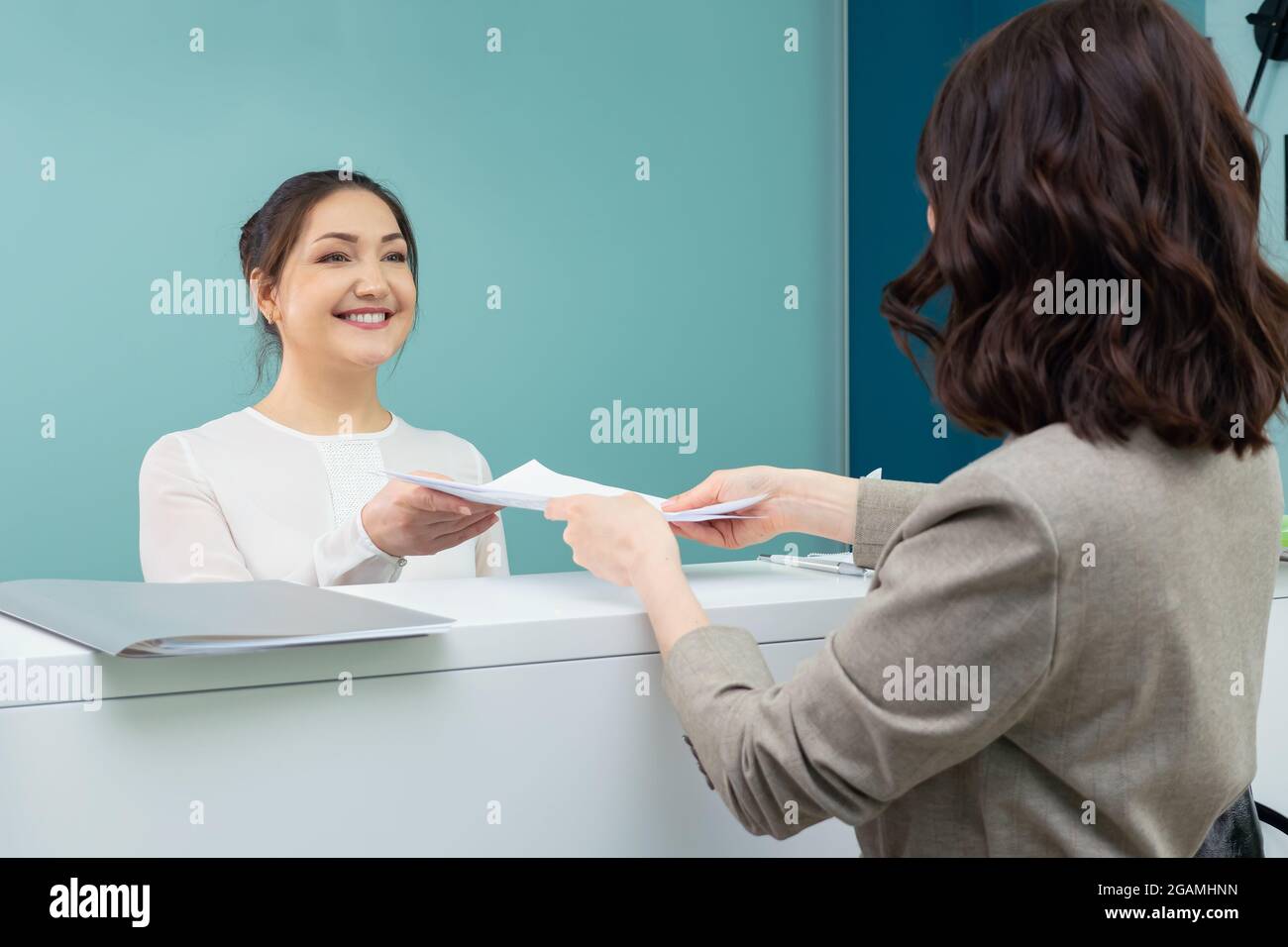 la receptionist accetta documenti da parte della visitatrice femminile Foto Stock