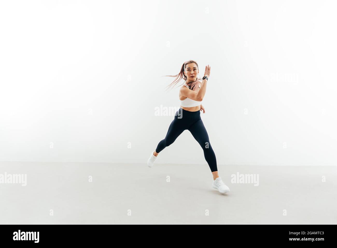 Giovane sportivo che corre in avanti all'interno. Muscolare femminile che si esercita contro una parete bianca. Foto Stock