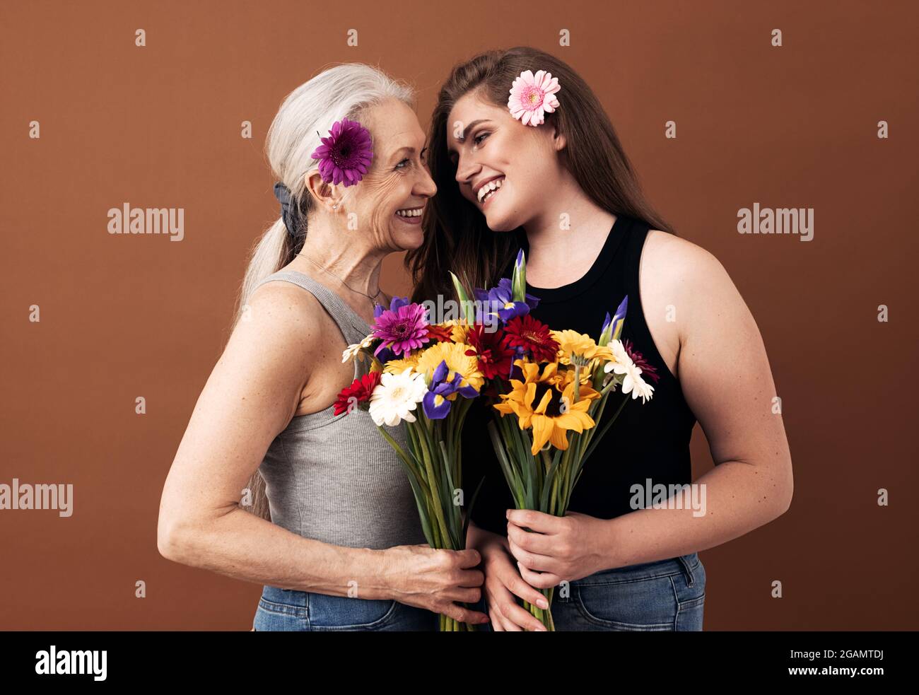 Due donne di diverse età con bouquet e fiori nei capelli che si guardano l'un l'altro Foto Stock