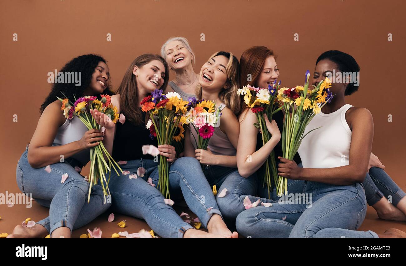 Sei donne di diverse età e tipi di corpo che tengono bouquet mentre si siedono in studio su uno sfondo marrone Foto Stock