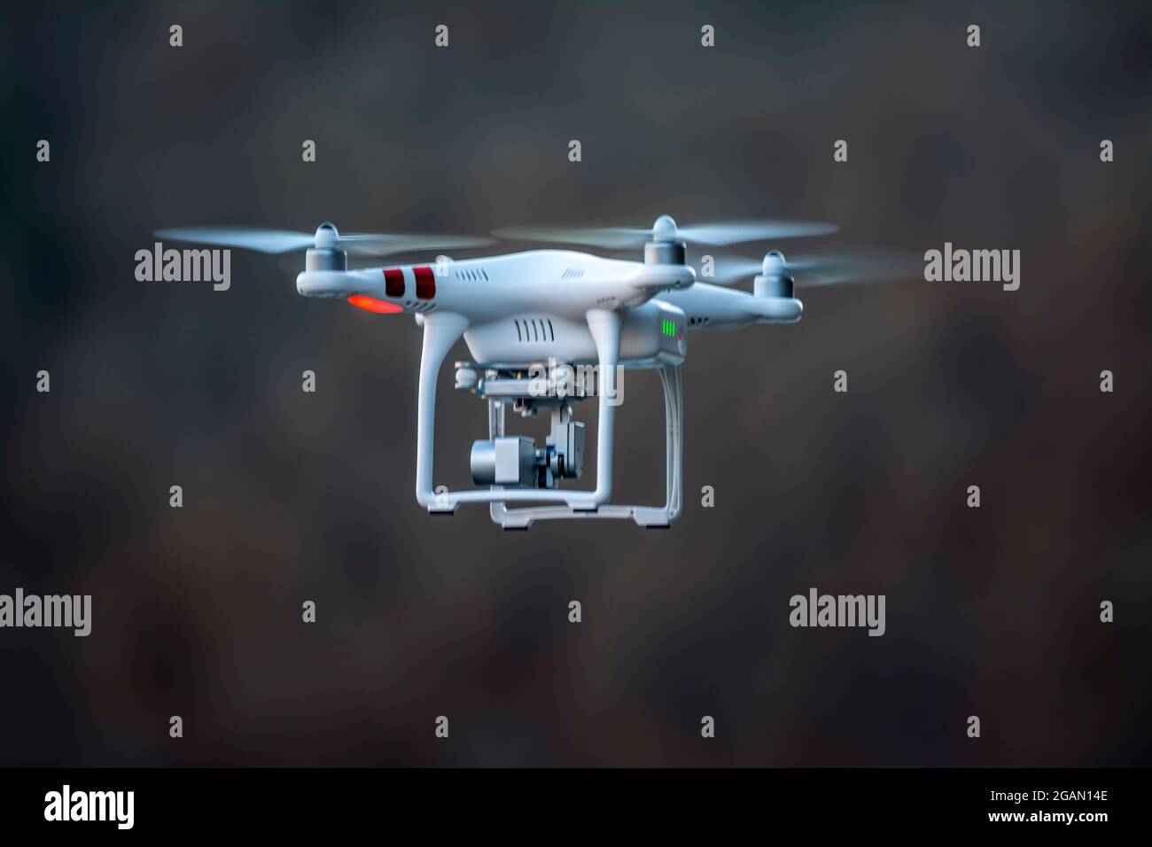 Un drone bianco che vola in aria durante il giorno con uno sfondo sfocato che mostra la natura e gli alberi nelle vicinanze Foto Stock