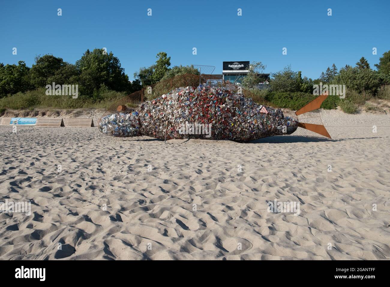 Pärnu, Estonia - 11 luglio 2021: Contenitore gigante di rifiuti a forma di pesce per la raccolta di rifiuti di plastica su una spiaggia pulita. Foto Stock