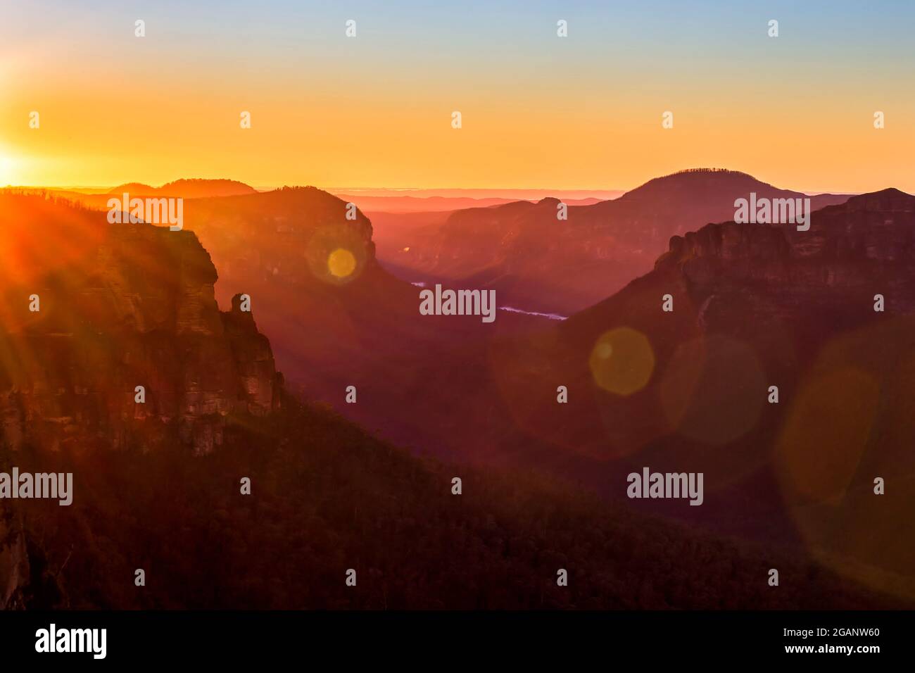 Raggi del sole che sorge intorno Pulpit Rock fuori Govetts salto Lookout nelle blu Montagne dell'Australia. Foto Stock