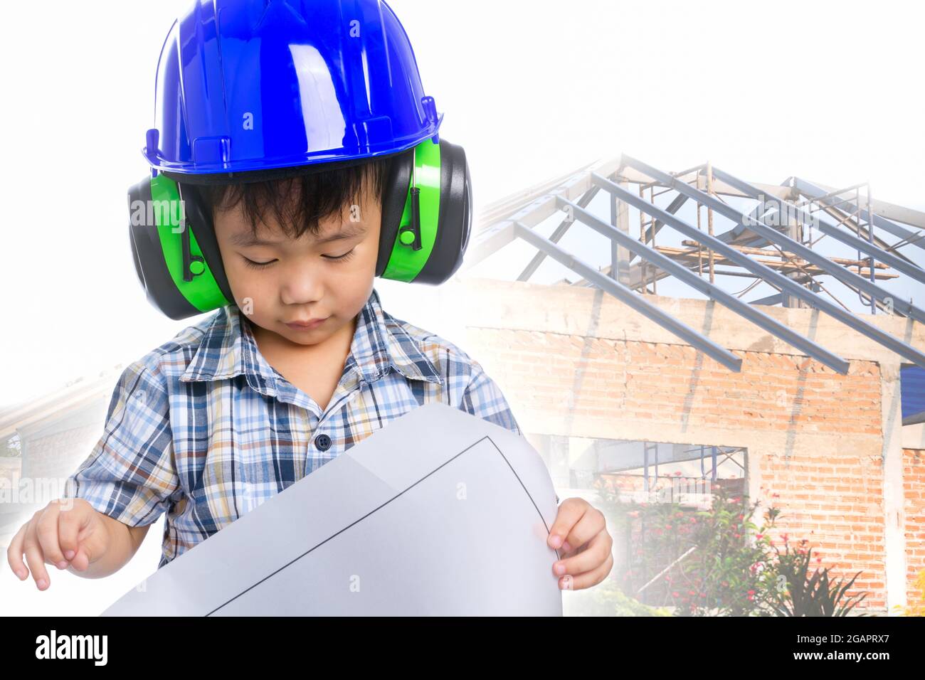 Sogno della carriera futura del bambino (ingegnere). Ragazzo asiatico (tailandese) con blueprint, indossando cuffie e casco blu, casa di mattoni ancora in costruzione Foto Stock