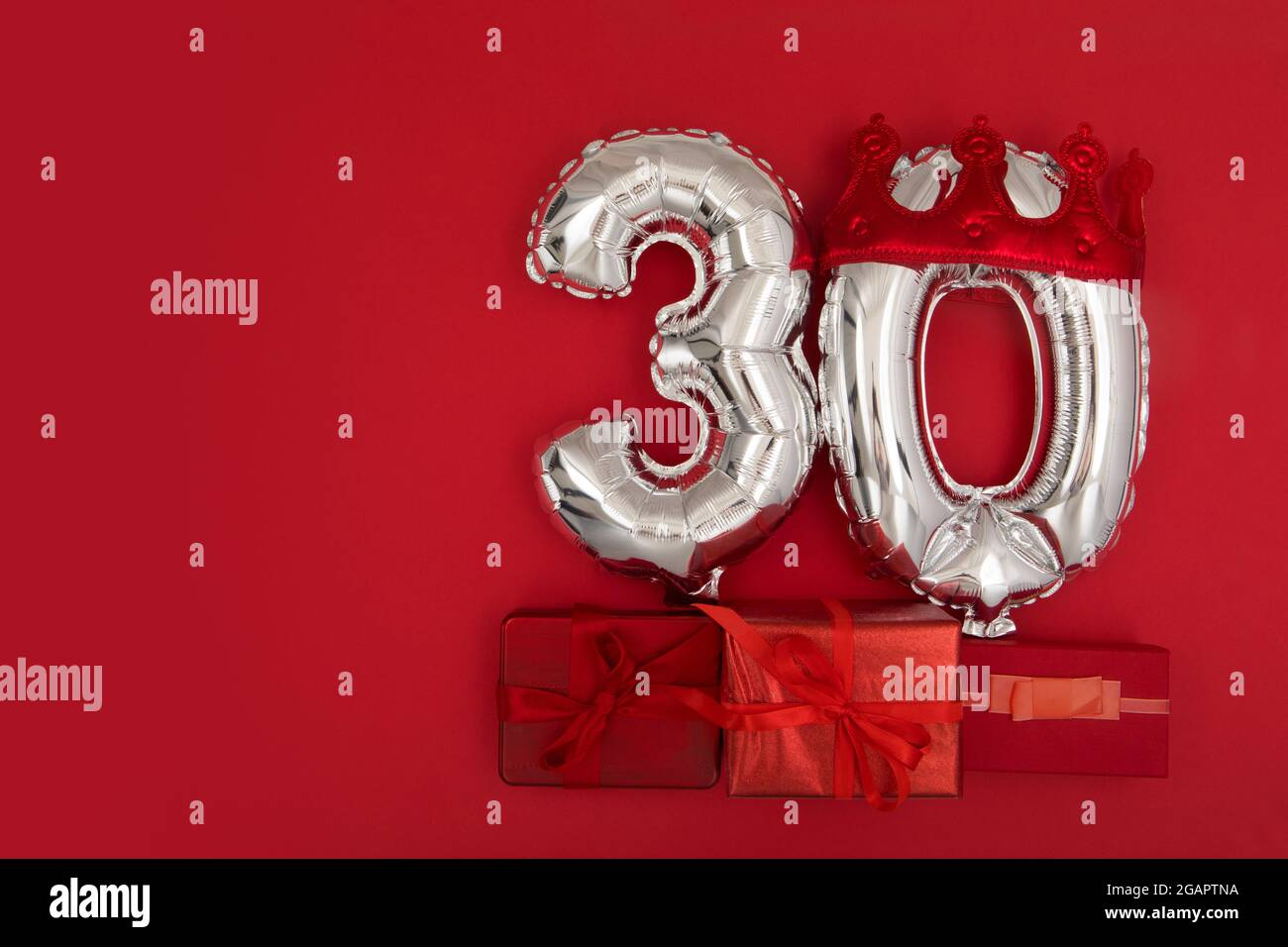 Palloncini d'aria in argento con il numero trenta posti su sfondo rosso con regali avvolti per il concetto di anniversario di compleanno Foto Stock