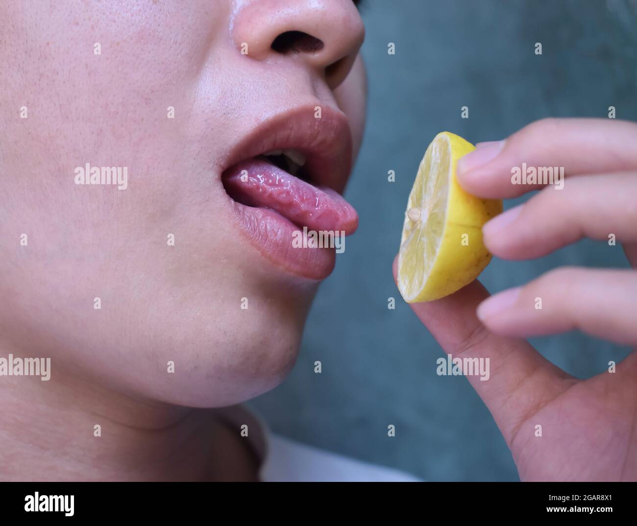 Sud-est asiatico, cinese e Myanmar giovane uomo con influenza fredda ottiene la perdita di gusto. Assaggia il limone mentre si trova a casa. Vista in primo piano. Foto Stock