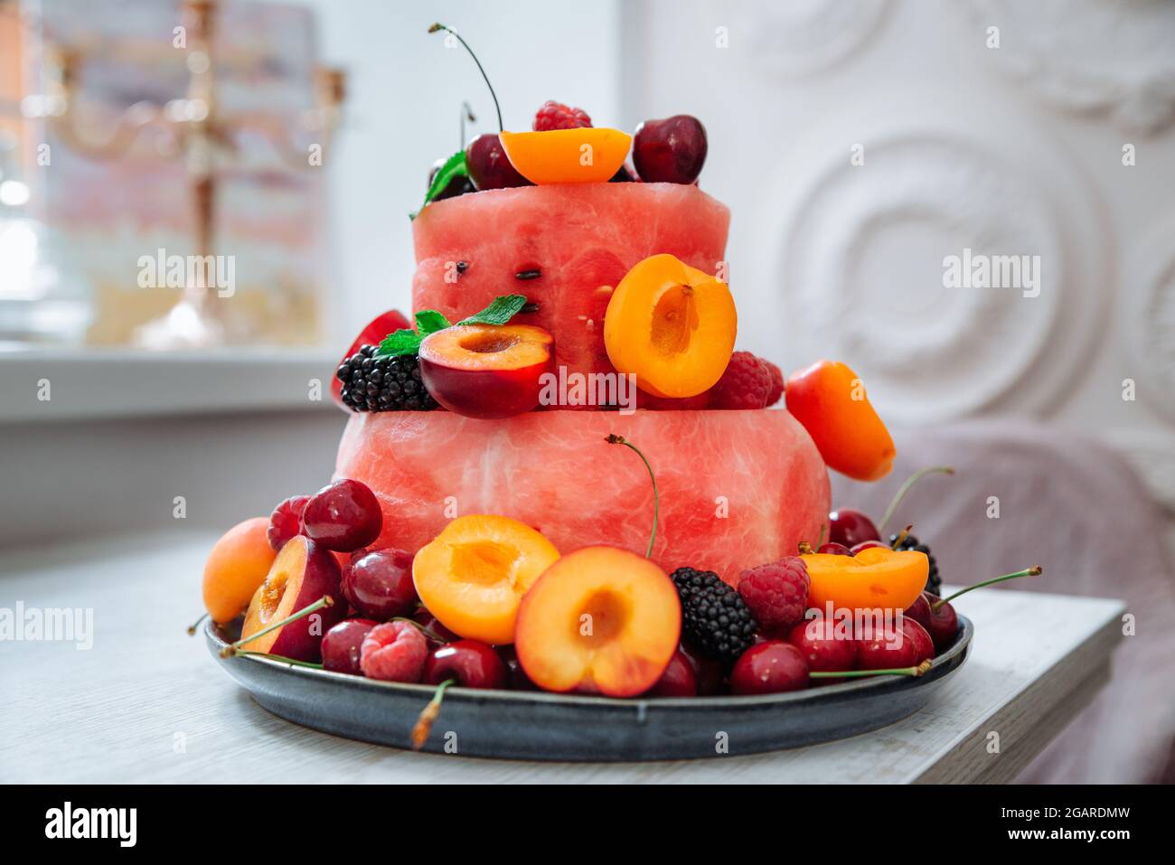 Torta multistrato di frutti di bosco e frutta. Macedonia di frutta fresca e bacche sotto forma di torta decorata con foglie di menta. Dessert estivo e vitamina conc Foto Stock
