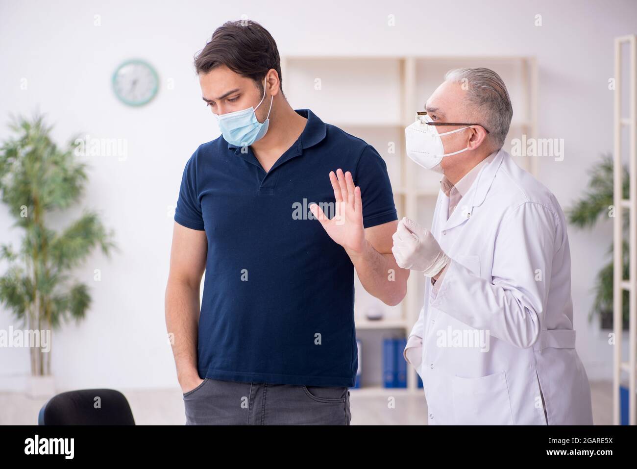Giovane paziente che visita il medico vecchio maschio durante la pandemia Foto Stock
