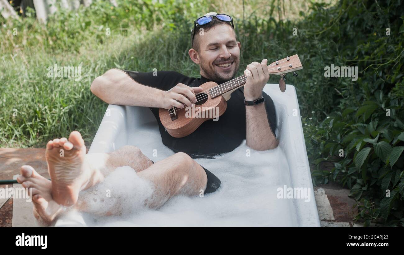 un uomo allegro nella vasca da bagno gioca l'ukulele Foto Stock