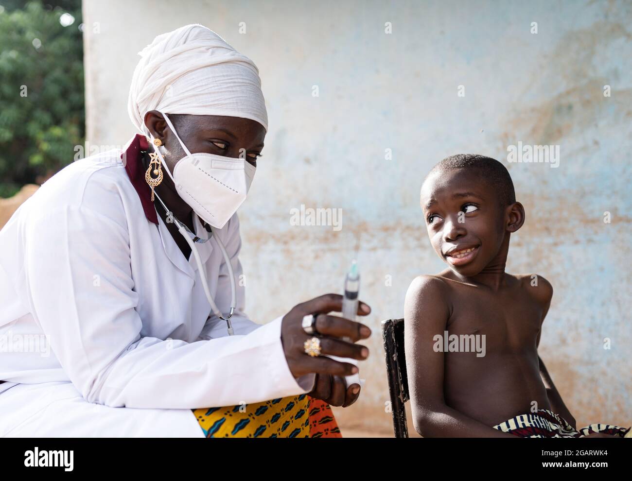 In questa immagine, un bambino africano carino sta scambiando le opinioni con il suo pediatra che sta per iniettare un vaccino nel suo braccio Foto Stock