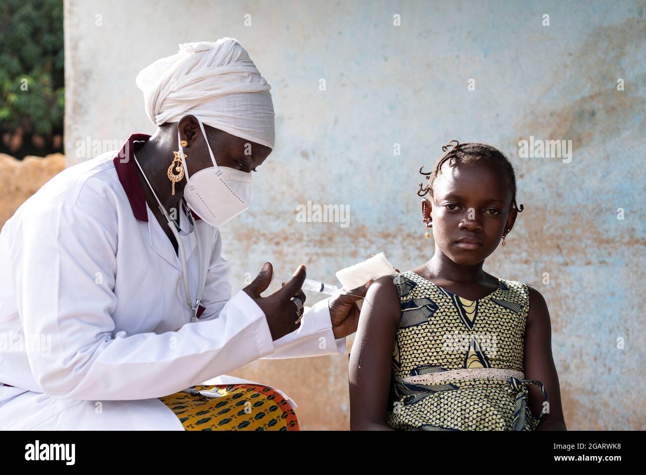 In questa immagine, una piccola studentessa africana tesa sta aspettando che il suo pediatra inietta una dose di vaccino nel suo braccio Foto Stock