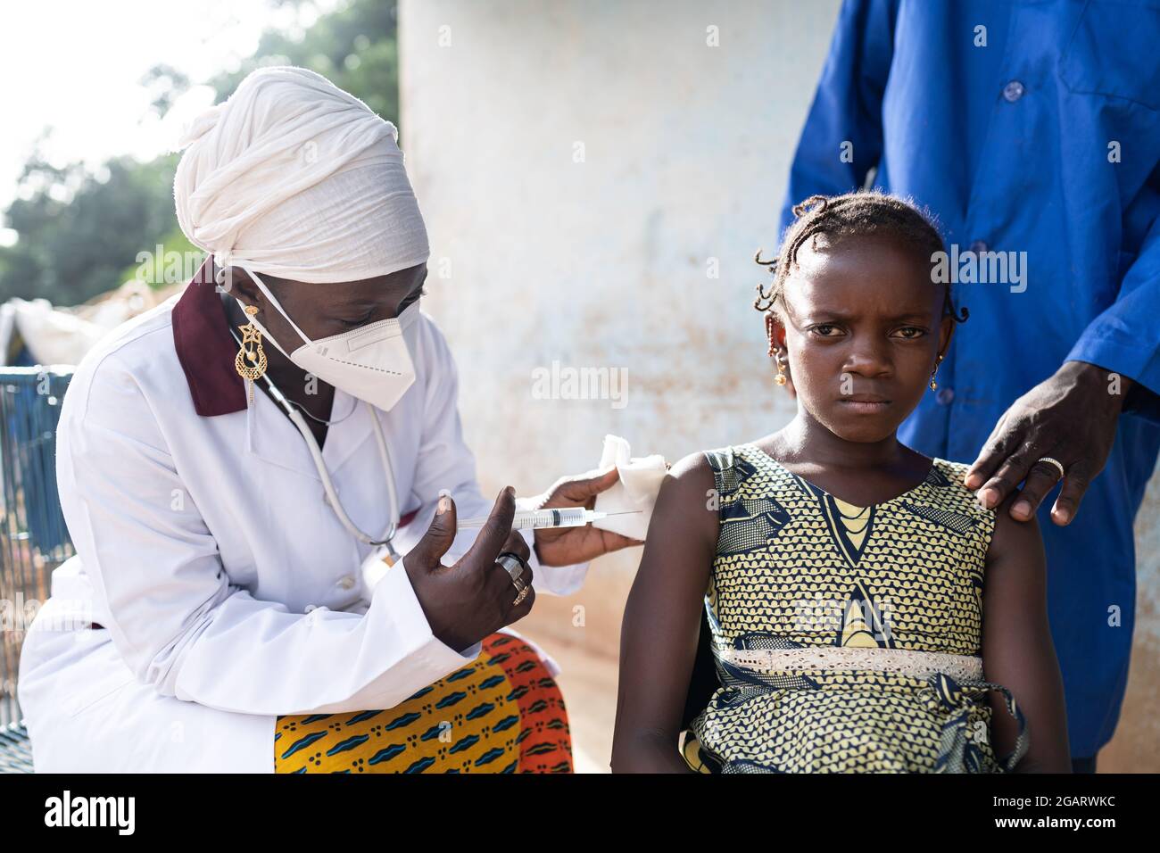 In questa immagine, una bambina africana preoccupata sta ricevendo una vaccinazione contro l'influenza da un infermiere nero con maschera protettiva per il viso Foto Stock