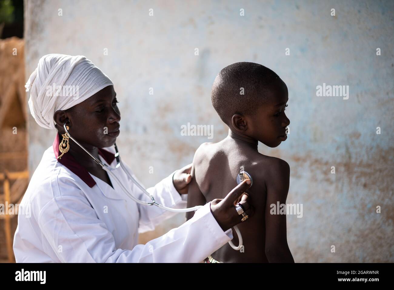 In questa immagine, un attento medico africano nero sta esaminando la funzione respiratoria e cardiaca di un piccolo bambino con uno stetoscopio Foto Stock