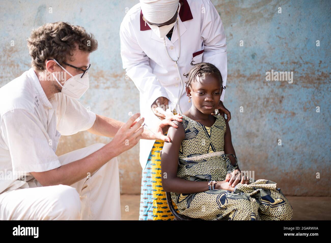In questa immagine, il personale medico di un dittario di villaggio africano che indossa maschere di protezione del viso sta vaccinando una bambina africana obedient d Foto Stock