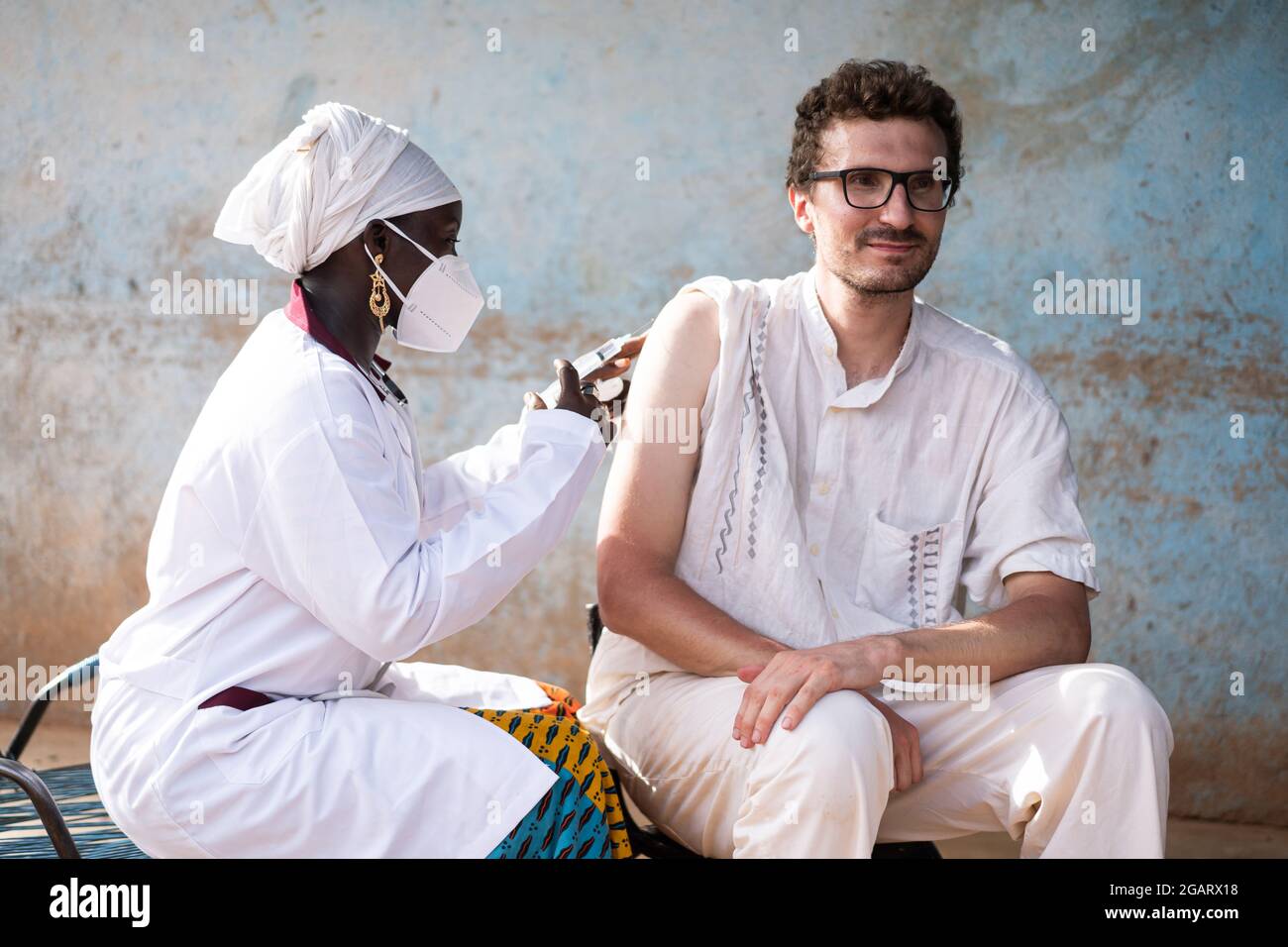 In questa immagine, un'infermiera nera che indossa una maschera facciale sta vaccinando un giovane uomo caucasico con un sorriso fiducioso sul viso contro la febbre gialla in un Foto Stock