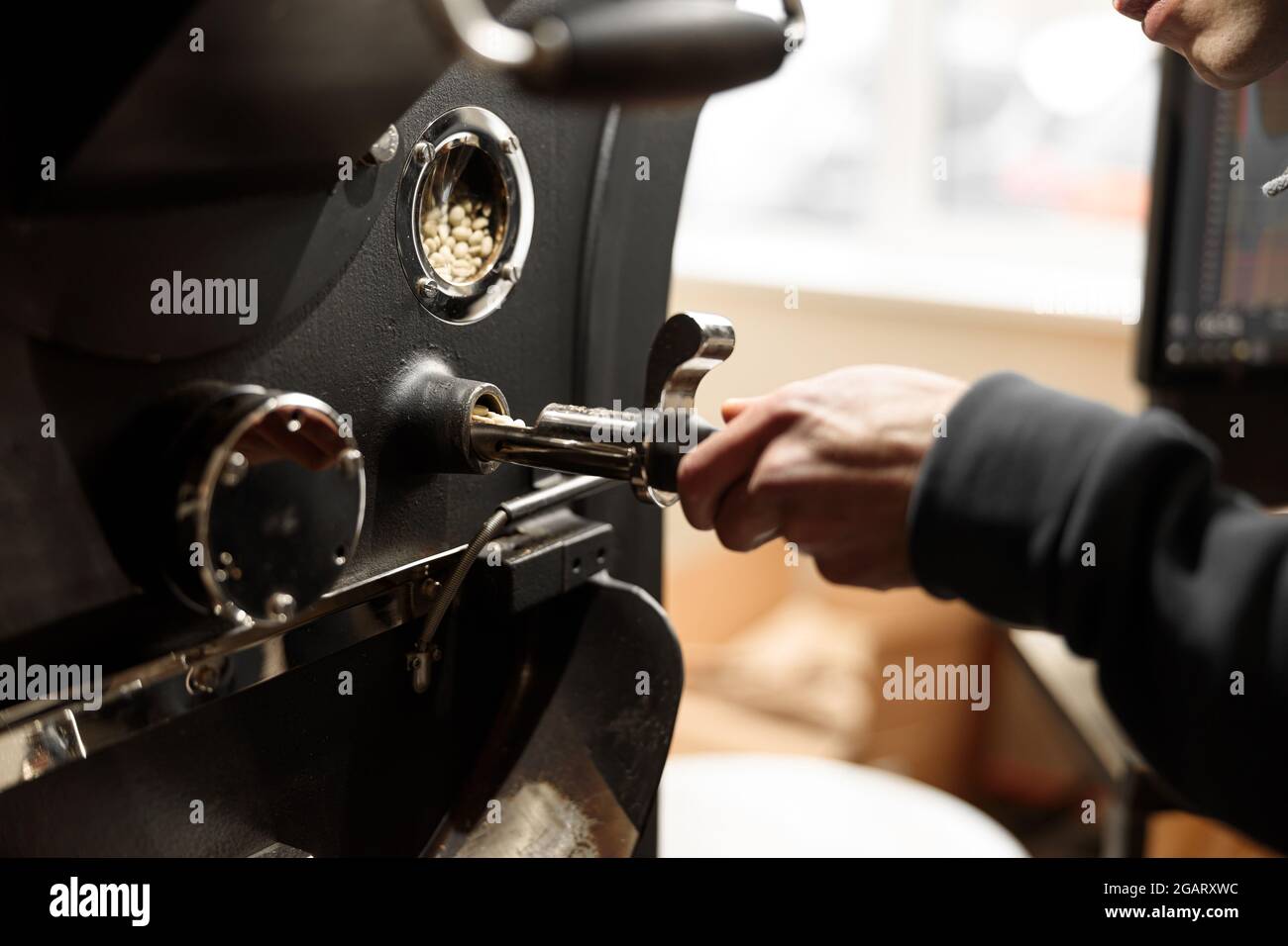 Un giovane lavoratore specializzato sta arrostendo il caffè nell'hangar Foto Stock
