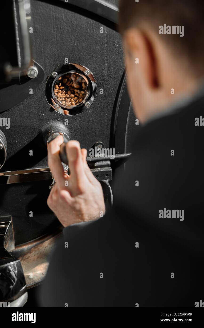 Un giovane lavoratore specializzato sta arrostendo il caffè nell'hangar Foto Stock