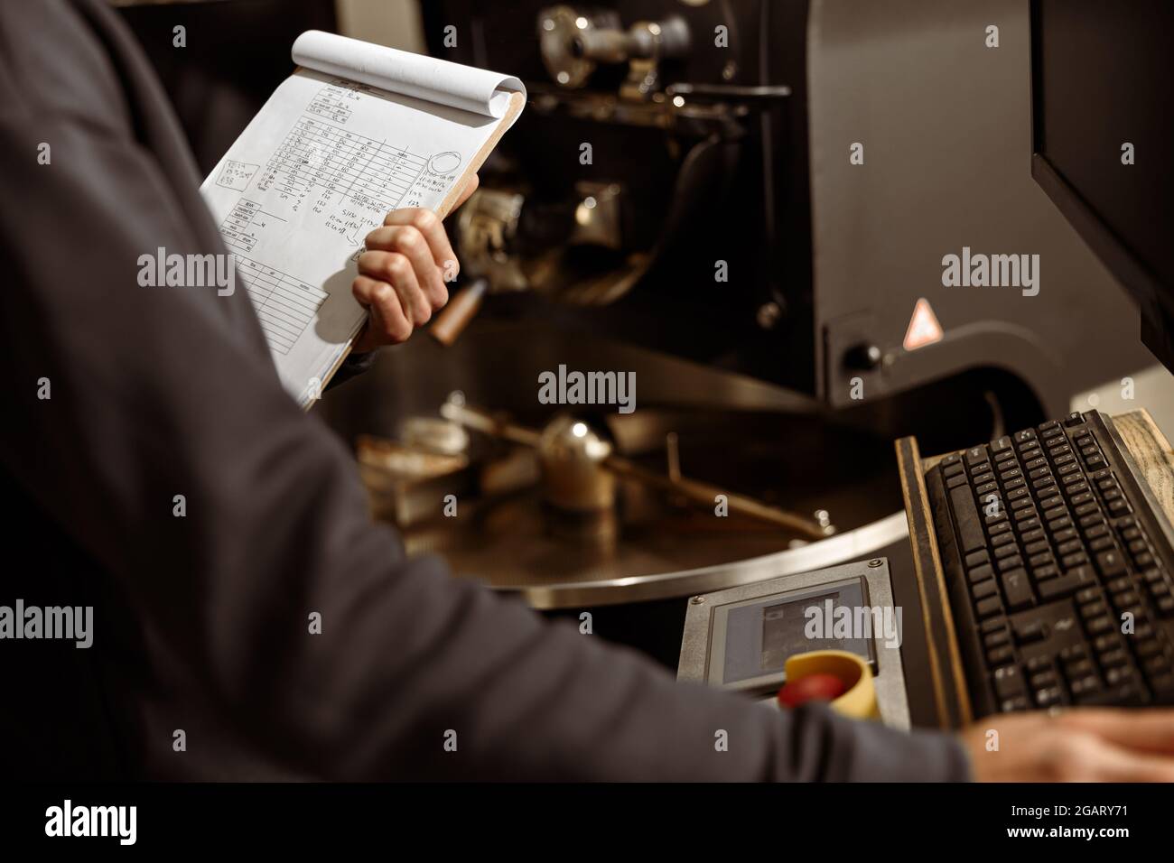 Un giovane lavoratore specializzato sta arrostendo il caffè nell'hangar Foto Stock
