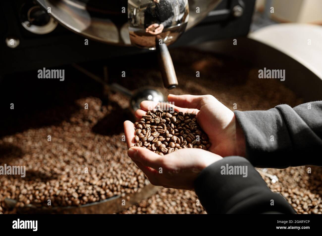 Un giovane lavoratore specializzato sta arrostendo il caffè nell'hangar Foto Stock