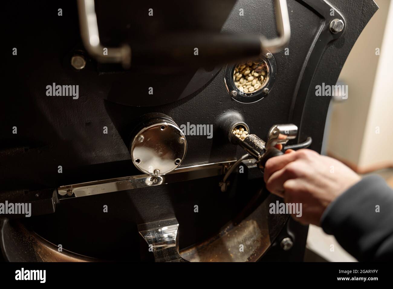 Un giovane lavoratore specializzato sta arrostendo il caffè nell'hangar Foto Stock