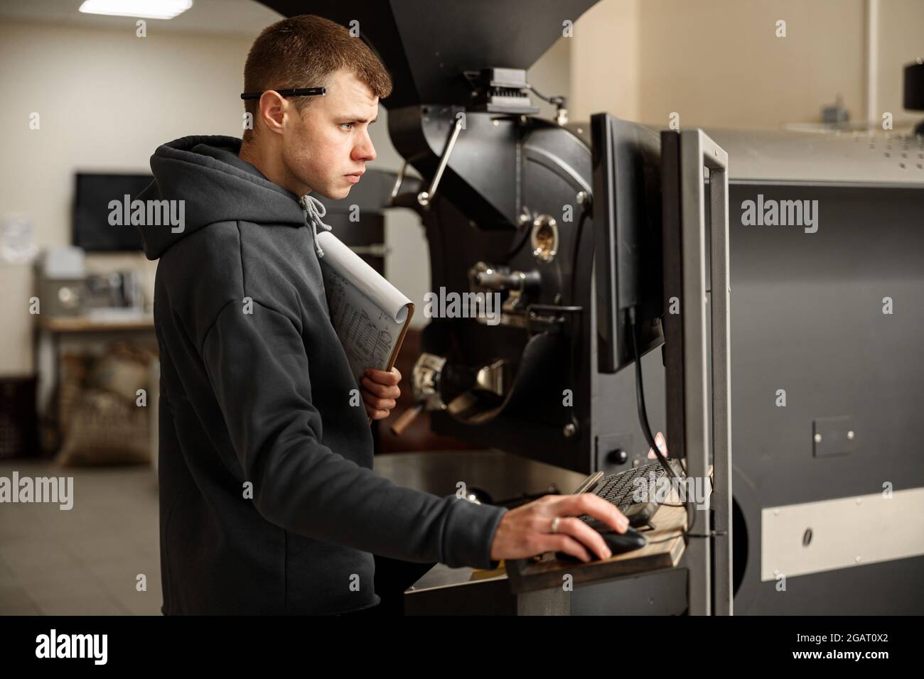 Un giovane lavoratore specializzato sta arrostendo il caffè nell'hangar Foto Stock