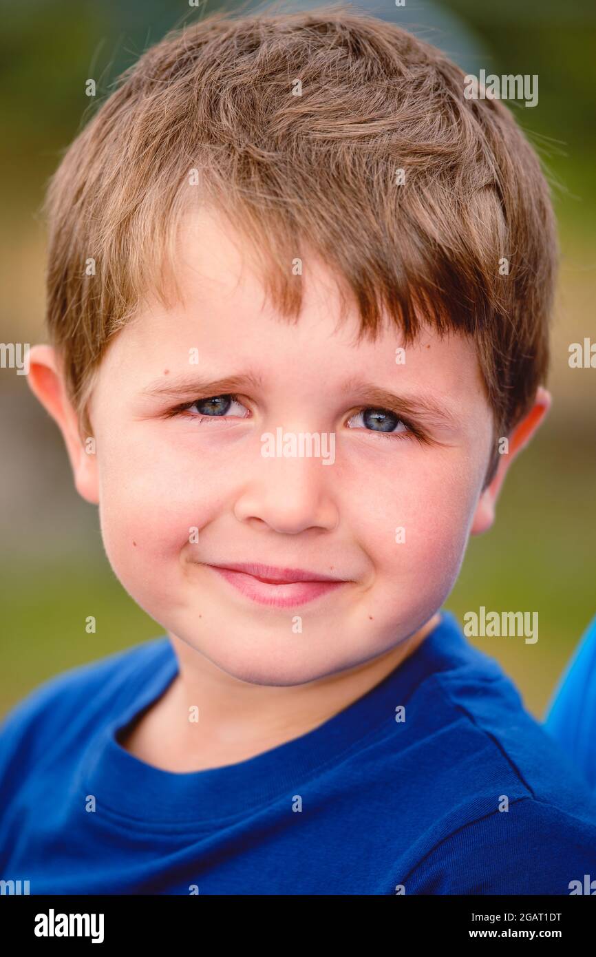 primo piano ritratto di allegro ragazzo caucasico di 7 anni sorridente con la bocca chiusa guardando la macchina fotografica. all'aperto profondità di campo poco profonda Foto Stock